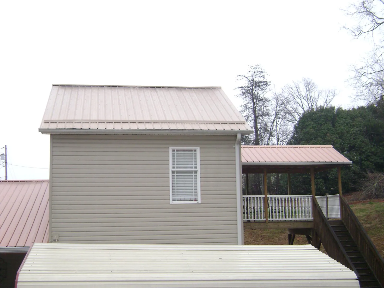 Tan metal roofs on a two story addition and attached porch, from a Roof Replacement job in Friendship
